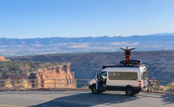 Un homme est debout sur le toit de son van, bras levés, face à un canyon